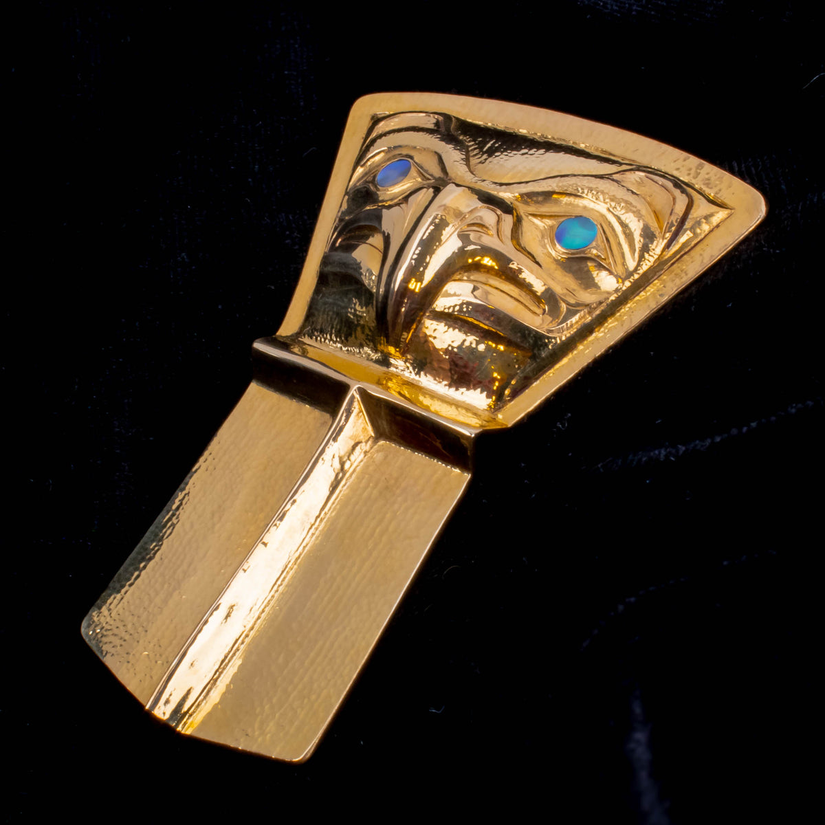 A close-up of a gold pendant in the shape of a shield on a a black background