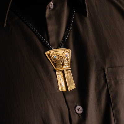 Close-up of a gold shield pendant on a black chain worn by a model