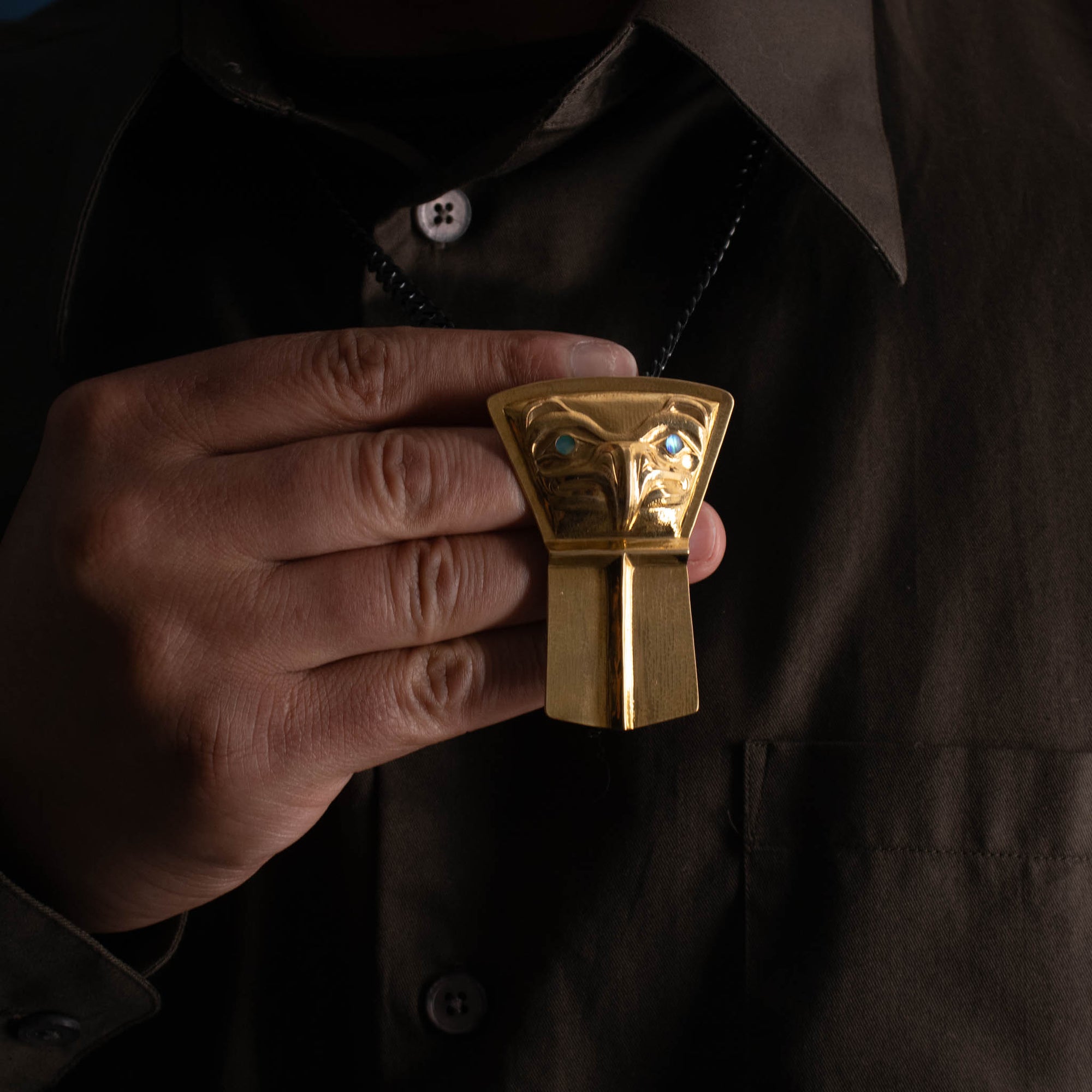 A male model holds a gold northwest coast shield pendant