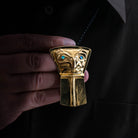 A male model holds a gold shield pendant with an eagle design and blue eyes