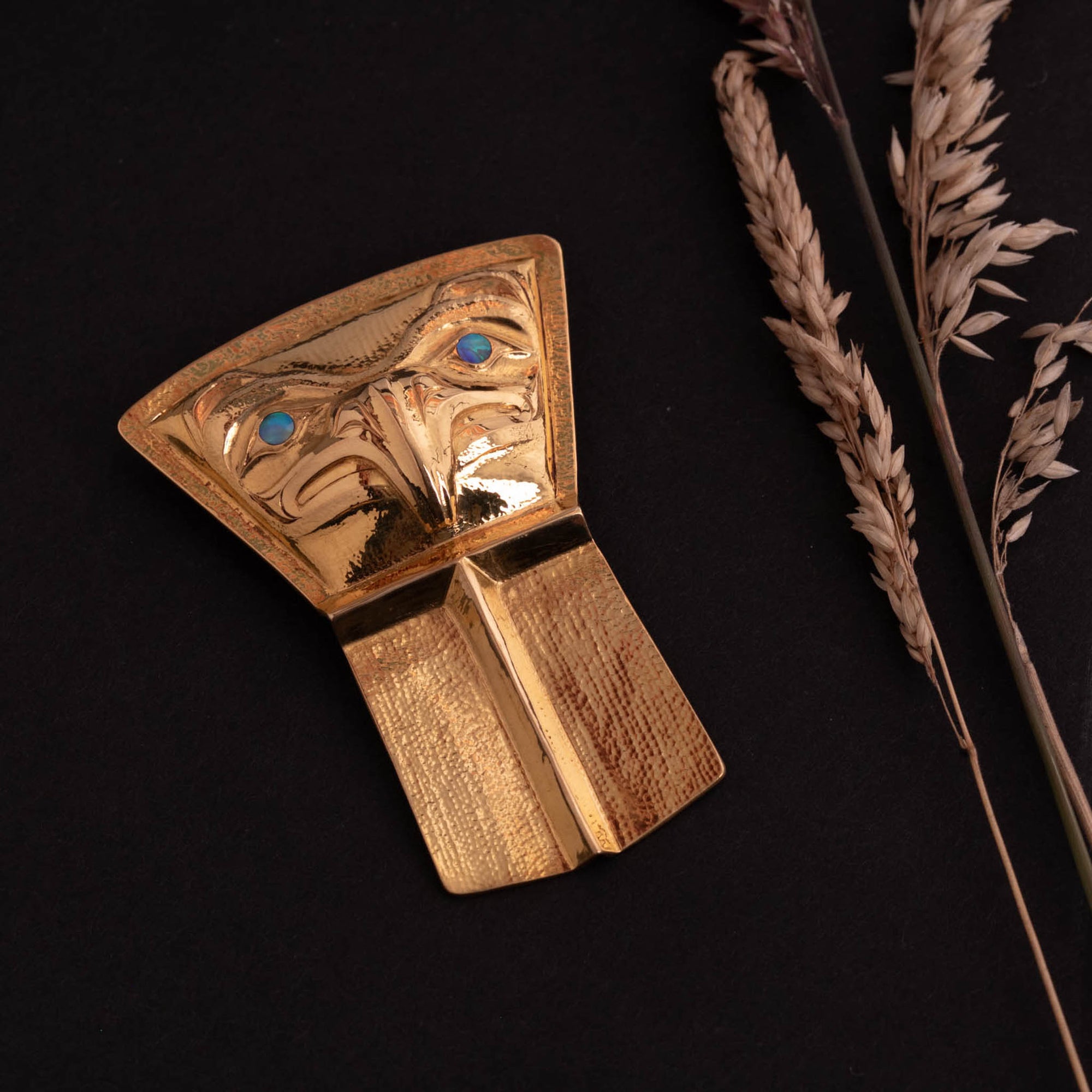 Gold northwest coast pendant with an eagle and abalone eyes with dried grass to the left
