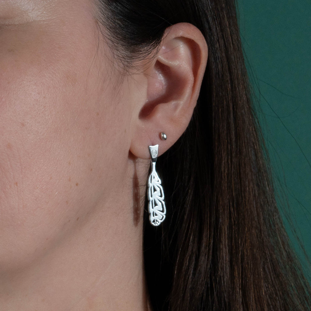 Close-up of a model's ear with dark hair wearing long silver earrings and a green background.