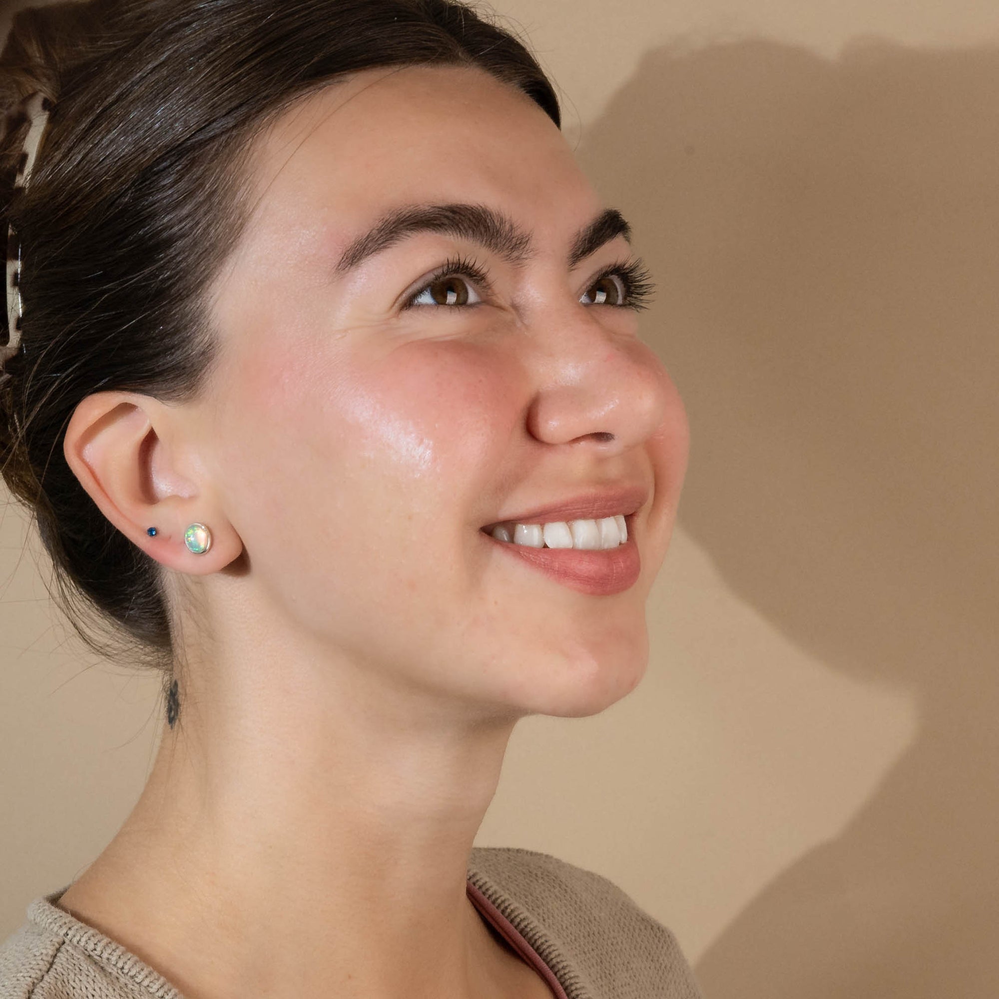 Model with brown hair facing to the right, smiling, wearing white opal studs.