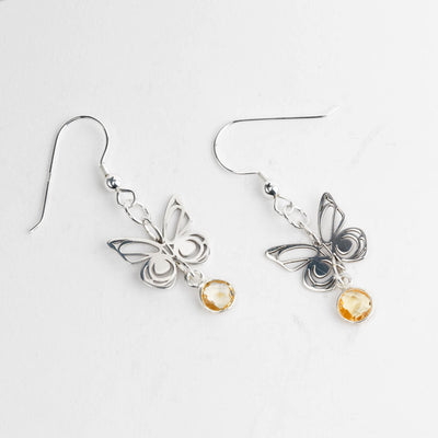 Butterfly-shaped earrings with small round faceted citrine stones on a light gray background.