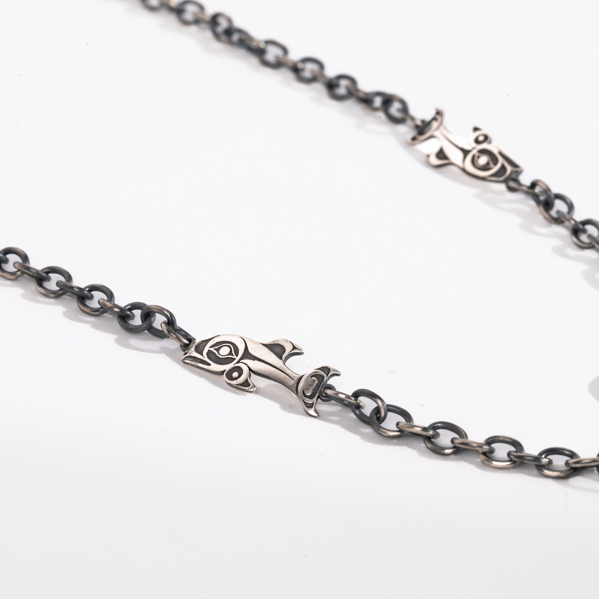 Close up of Salmon and chain links of Sterling Silver Killer whale and salmon necklace hand made by Ts'msyen artist Morgan Asoyuf on a white background
