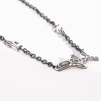 Angled shot of Sterling Silver Killer whale and salmon necklace hand made by Ts'msyen artist Morgan Asoyuf on a white background