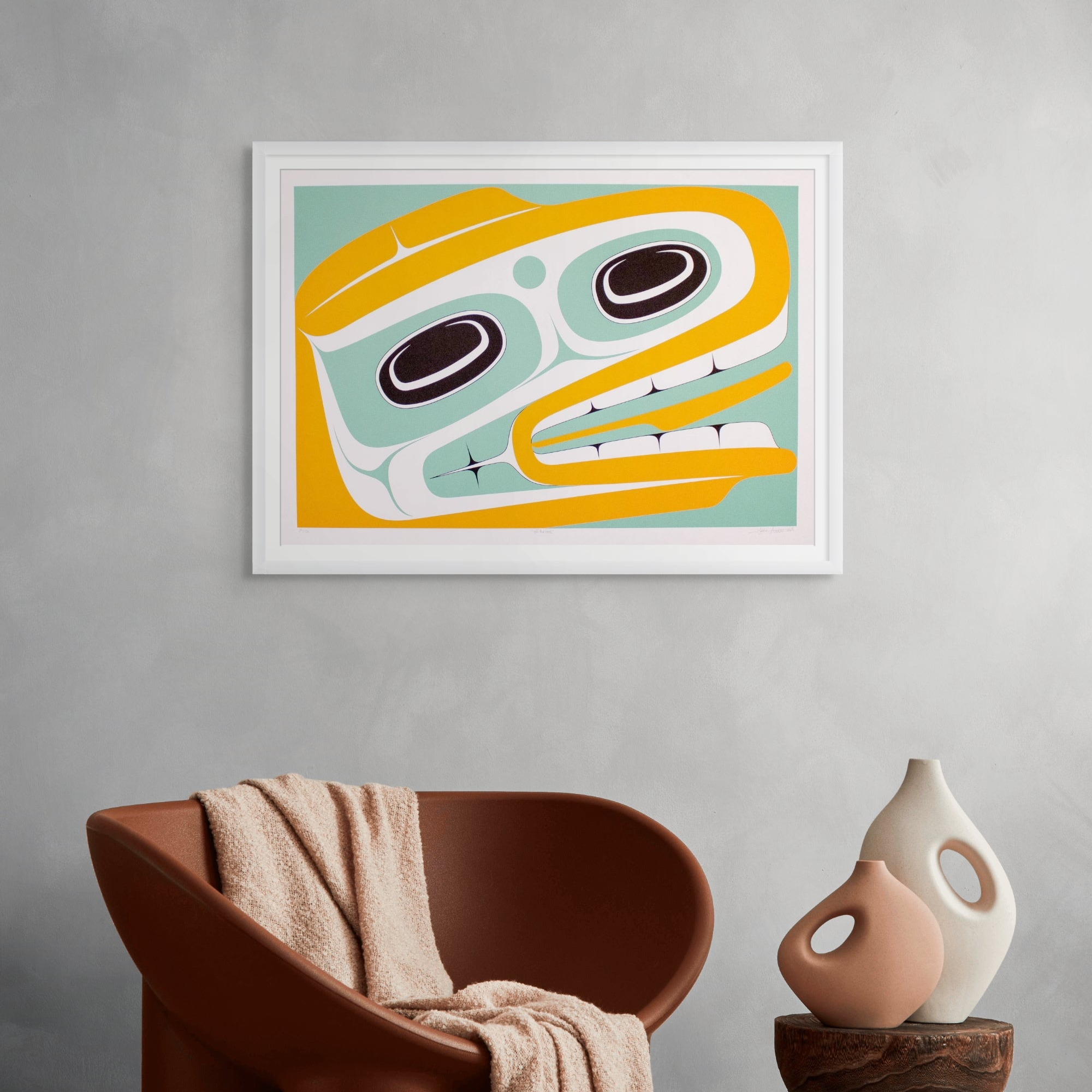 Framed abstract art piece on a gray wall with a brown chair and white vase below.
