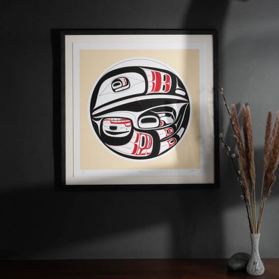 Framed artwork with a stylized formline  raven design on a beige background, placed on a dark surface.