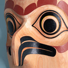Close-up of a wooden owl mask with intricate carvings on a blue background showing the depth of the owls beak.