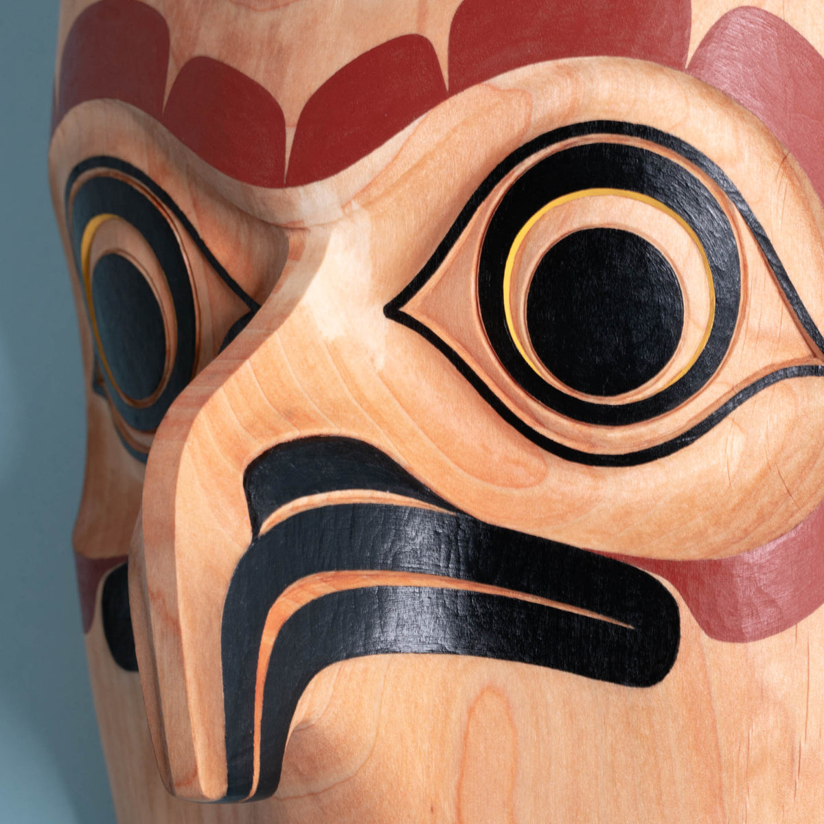Close-up of a wooden owl mask with intricate carvings on a blue background showing the depth of the owls beak.