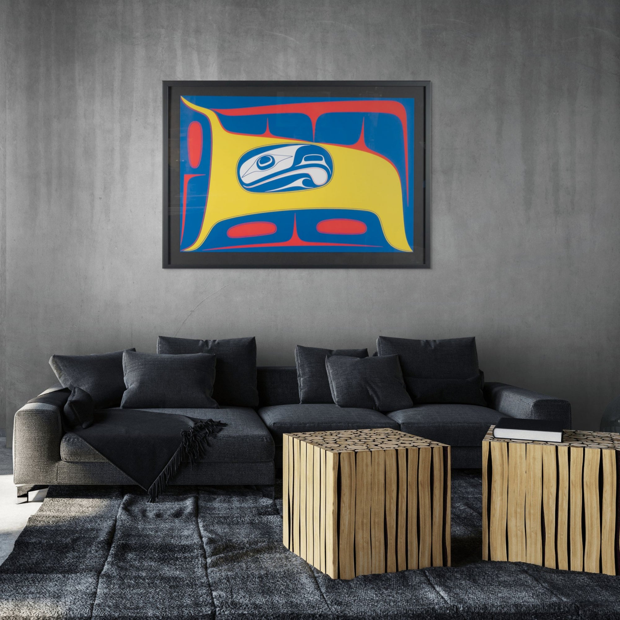 Modern living room with a gray sofa, abstract Framed fine artwork with a stylized formline design featuring a blue and white abstract eagle figure with yellow and red background by renowned haida artist Robert Davidson on the wall, and wooden side tables.