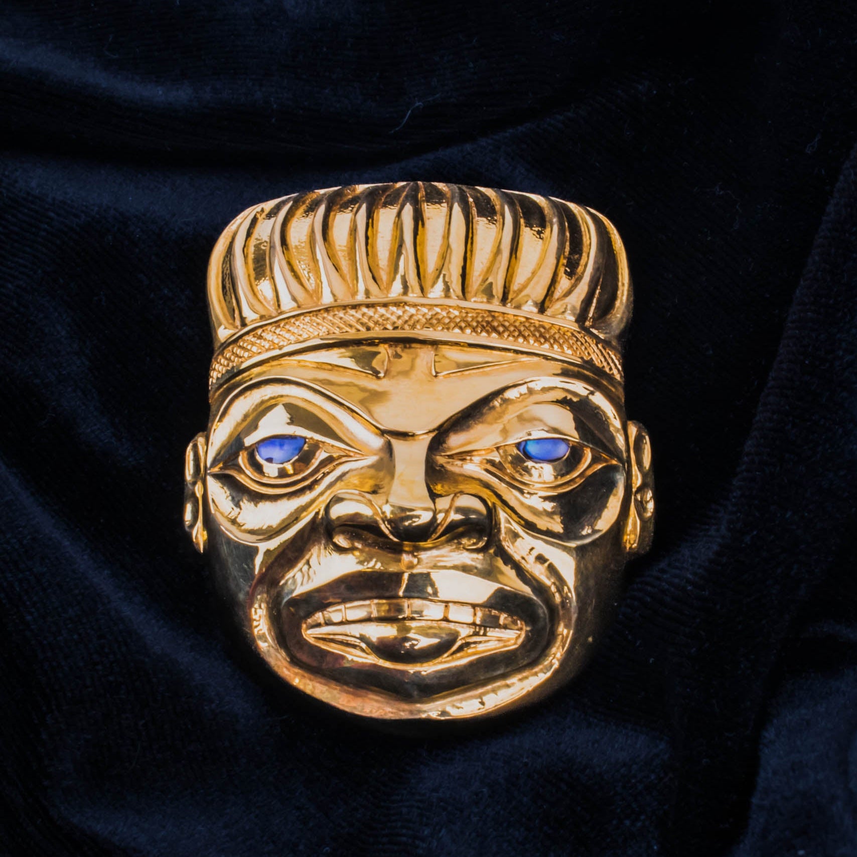 Gold pendant of a Shaman with blue abalone shell eyes on a black velvet background