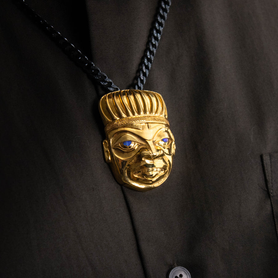 Close-up of a gold shaman pendant on a black chain worn by a model
