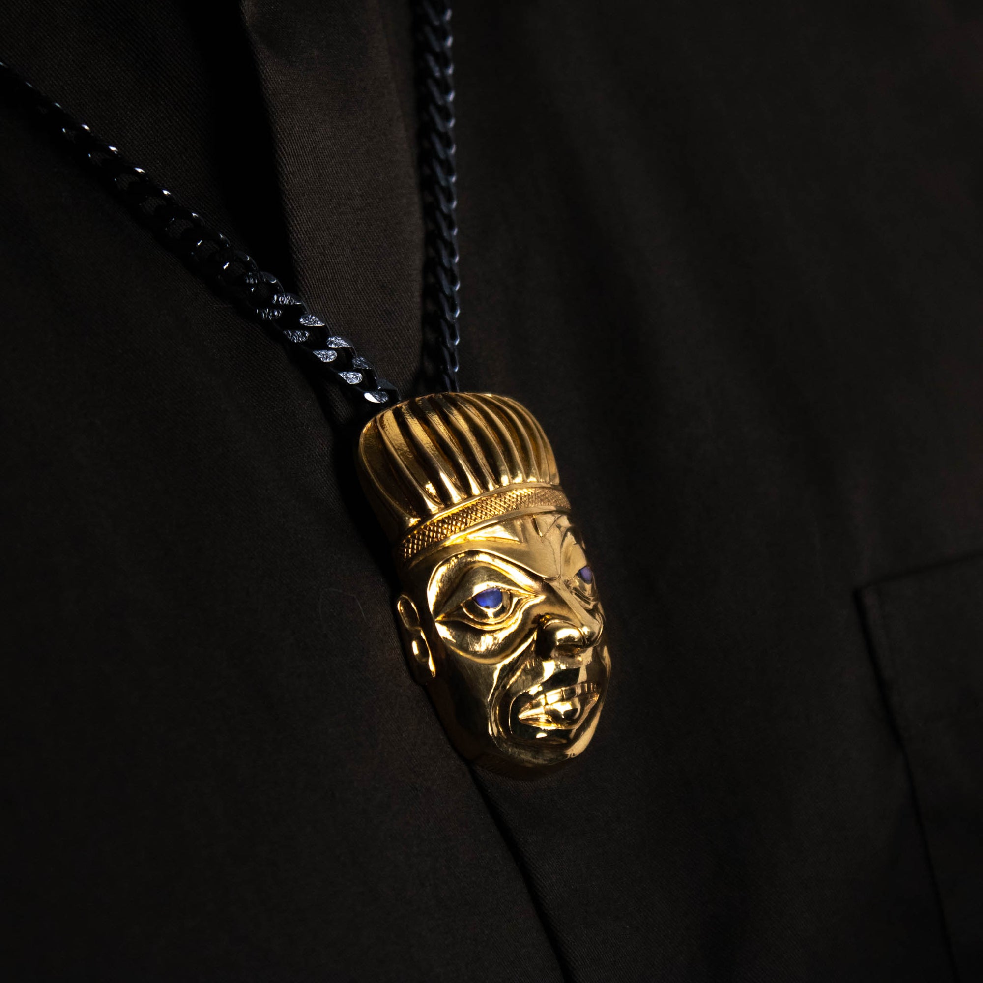 Left side close-up profile of Gold Shaman pendant worn by a model with a brown shirt