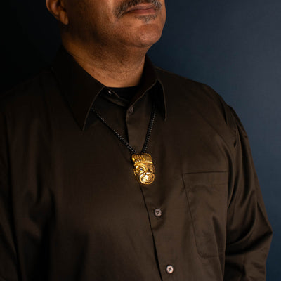 Gold pendant on a black chain worn by a man with a brown shirt