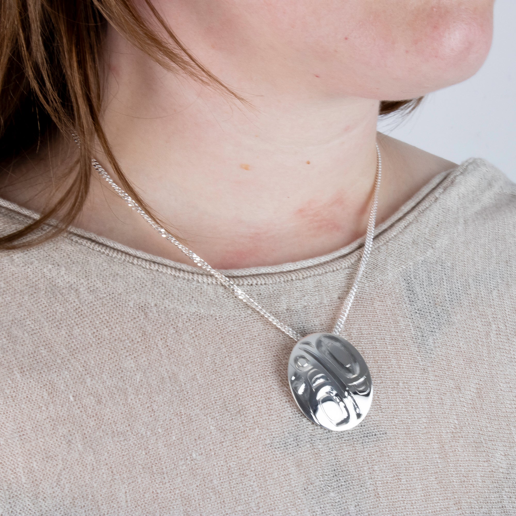 Haida Carver and Jeweller Alvin Adkins Sterling Silver Raven Pendant with 3mm curb chain on model side angle