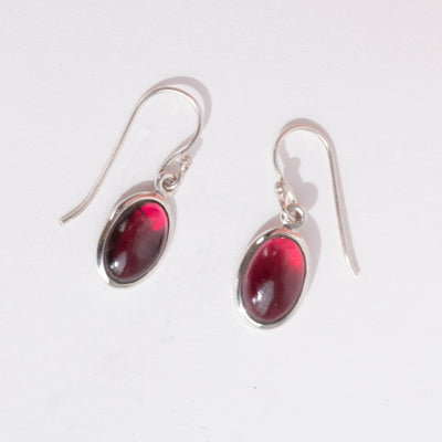 A pair of light red garnet dangle earrings on an angle with a white background.