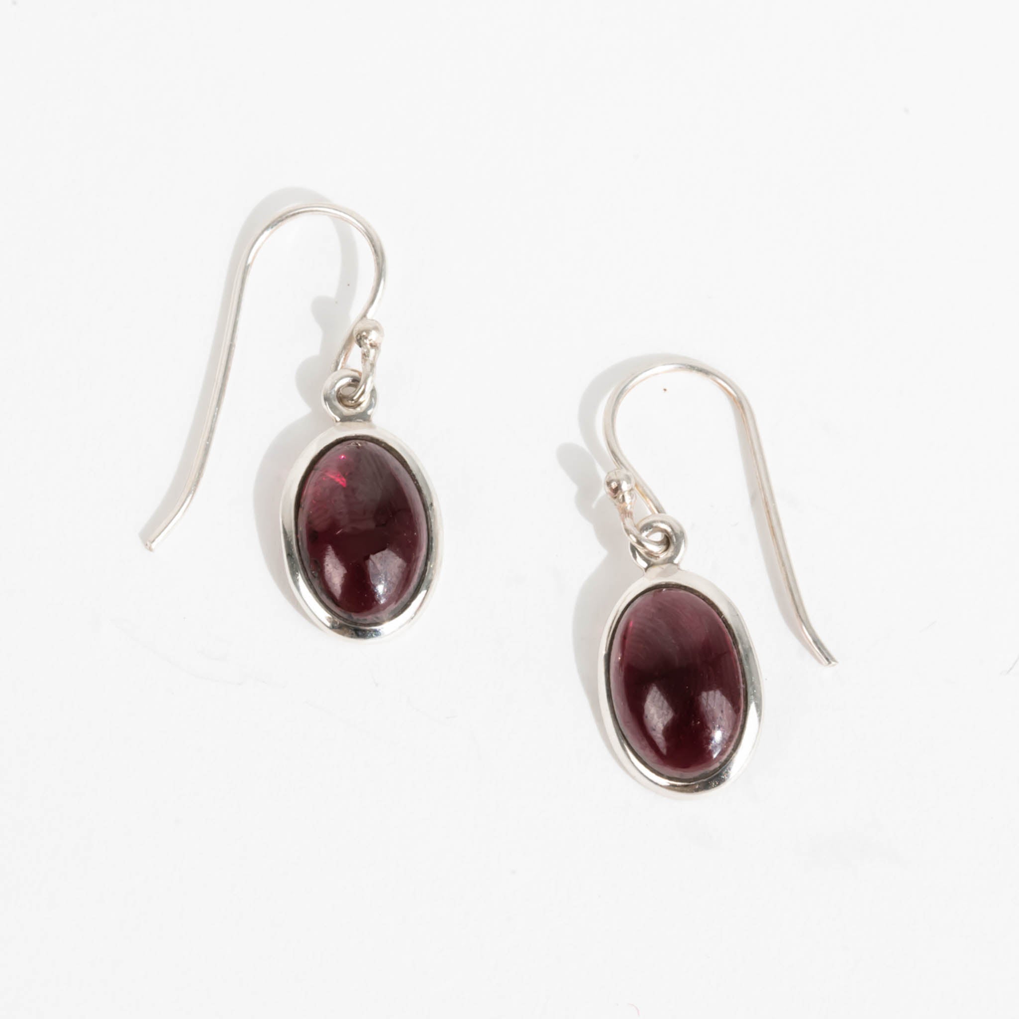 A pair of dark red oval garnet earrings with shepherd hooks on a white background 