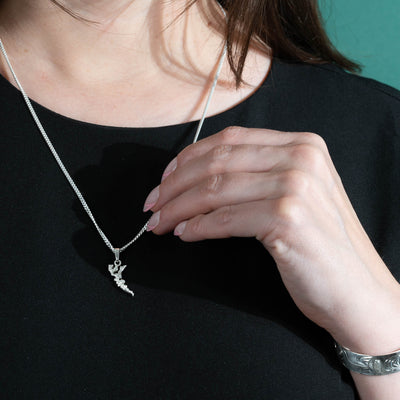 Woman wearing a silver chain and island shaped pendant with her left hand touching the chain.