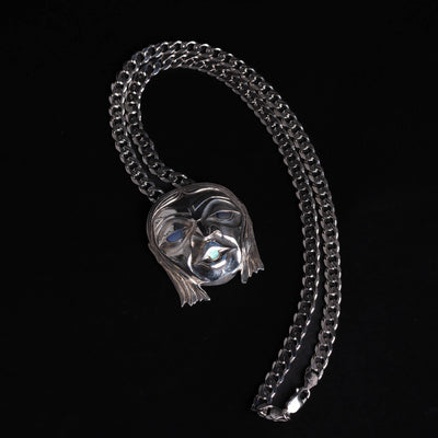 Silver mask pendant with glowing blue in the eyes and mouth with a silver chain on a black background.