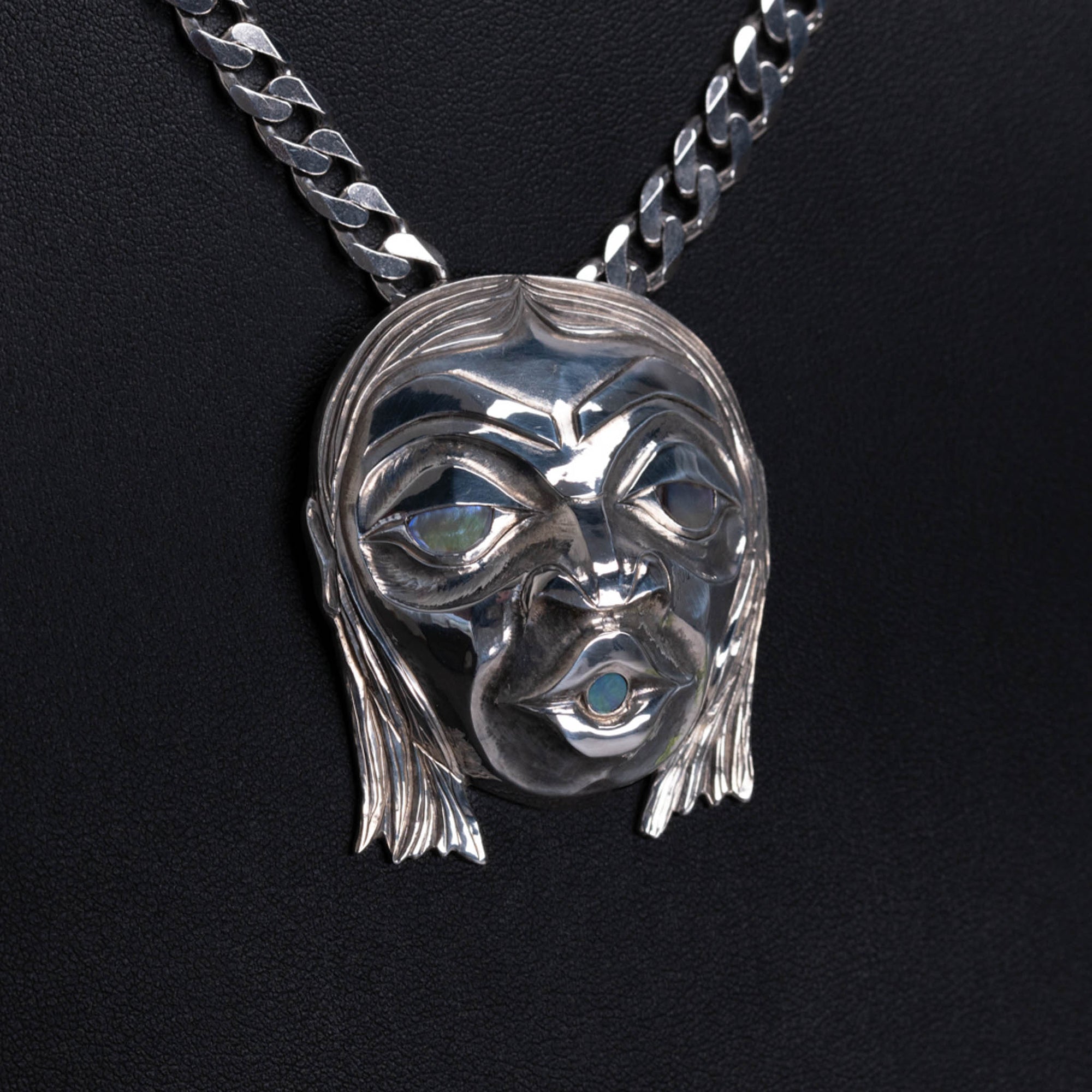 sterling silver pendant of a face with glowing shell in the eyes and mouth, hanging on a silver chain, with a black background.