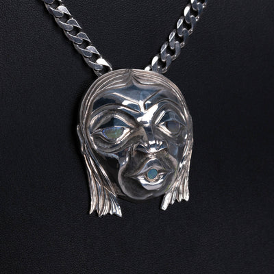 sterling silver pendant of a face with glowing shell in the eyes and mouth, hanging on a silver chain, with a black background.