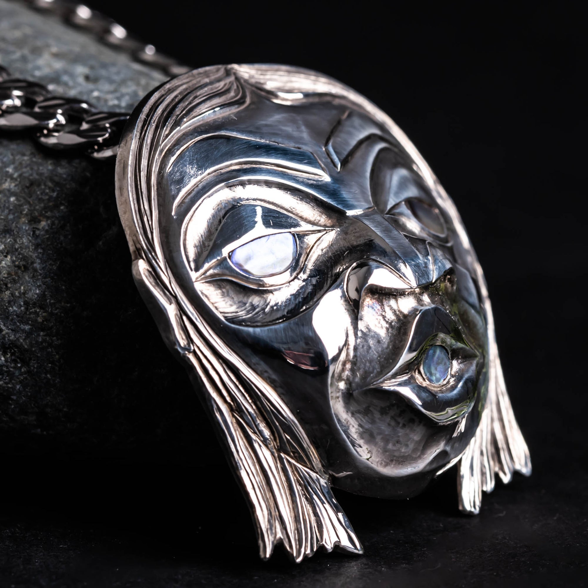 Silver head pendant with long hair close up on a dark background.