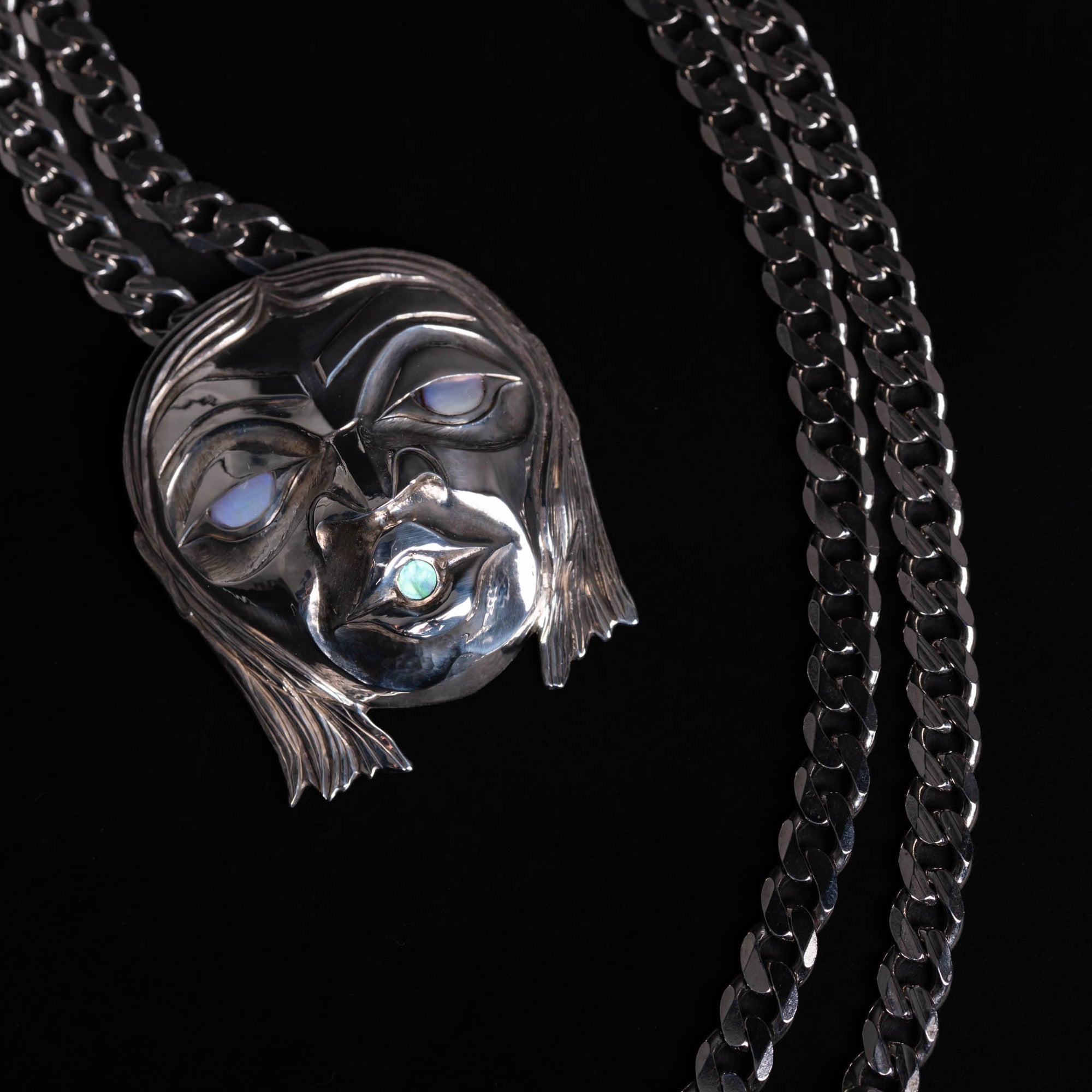 Silver mask pendant with silver chain on a black background.