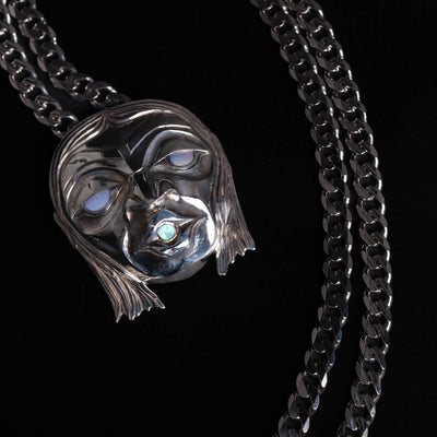Silver mask pendant with silver chain on a black background.