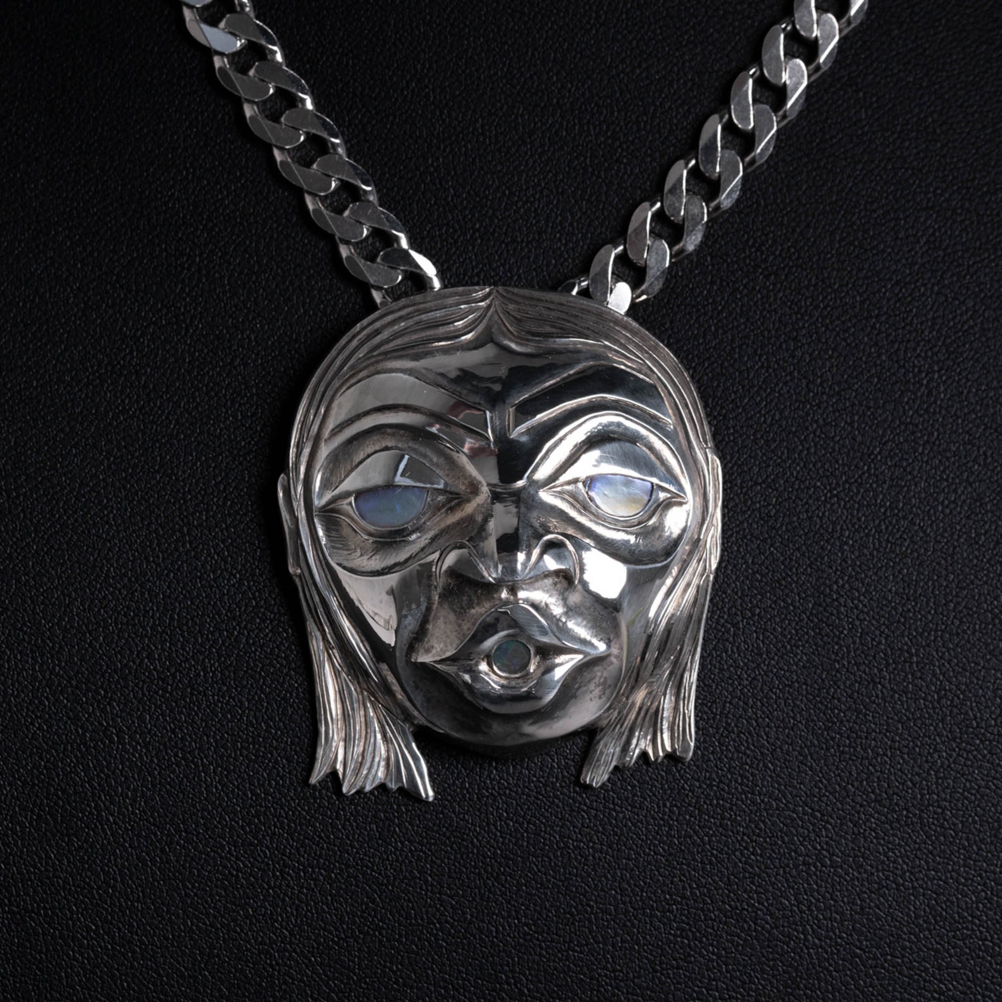 Silver face necklace on a black background.
