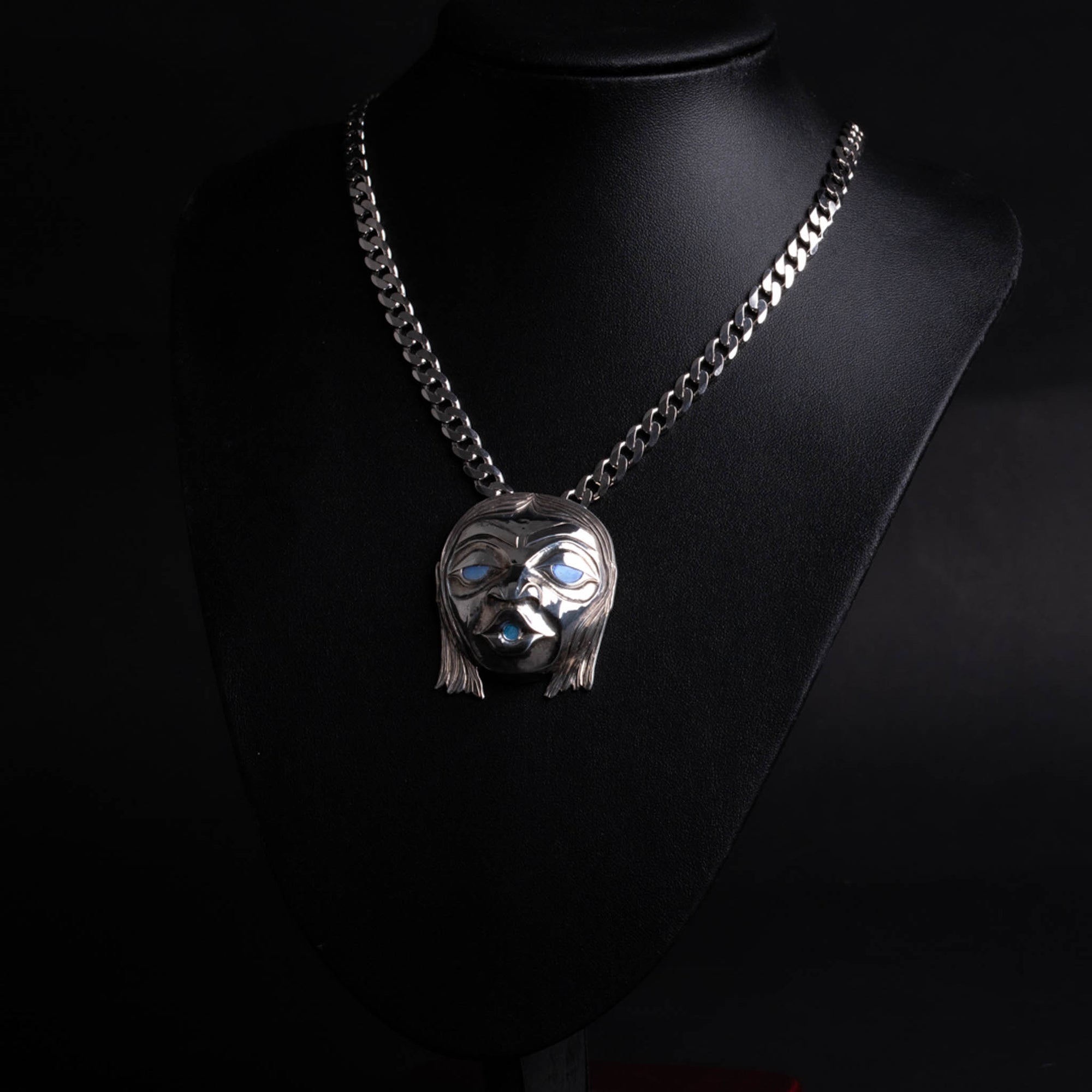 Silver face pendant with chain on a black mannequin against a black background