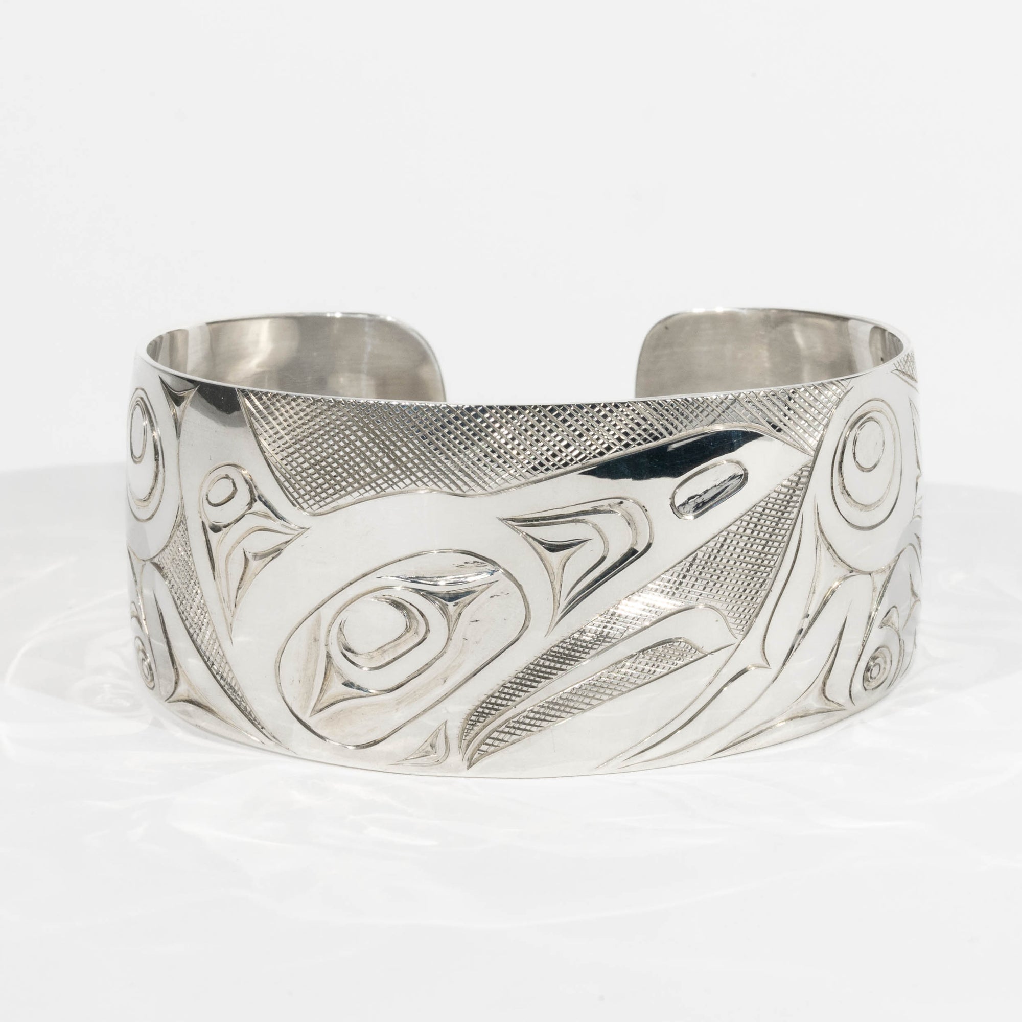 Front of Sterling Silver Haida Raven bracelet with intricate formline designs hand carved by James Sayer Haida Jeweller on a white background