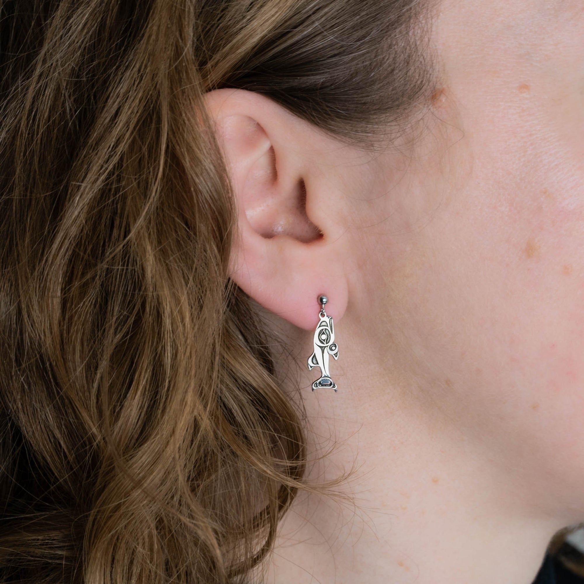 Close-up of a person wearing a silver  salmon stud earring.