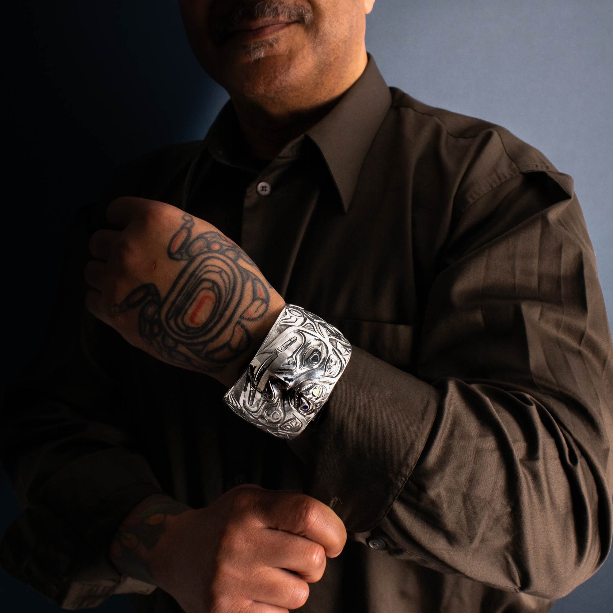 Man wearing a dark shirt with a silver bracelet on his wrist, against a dark background