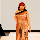 Model on the runway wearing long pink earrings and a long sparkly dress.