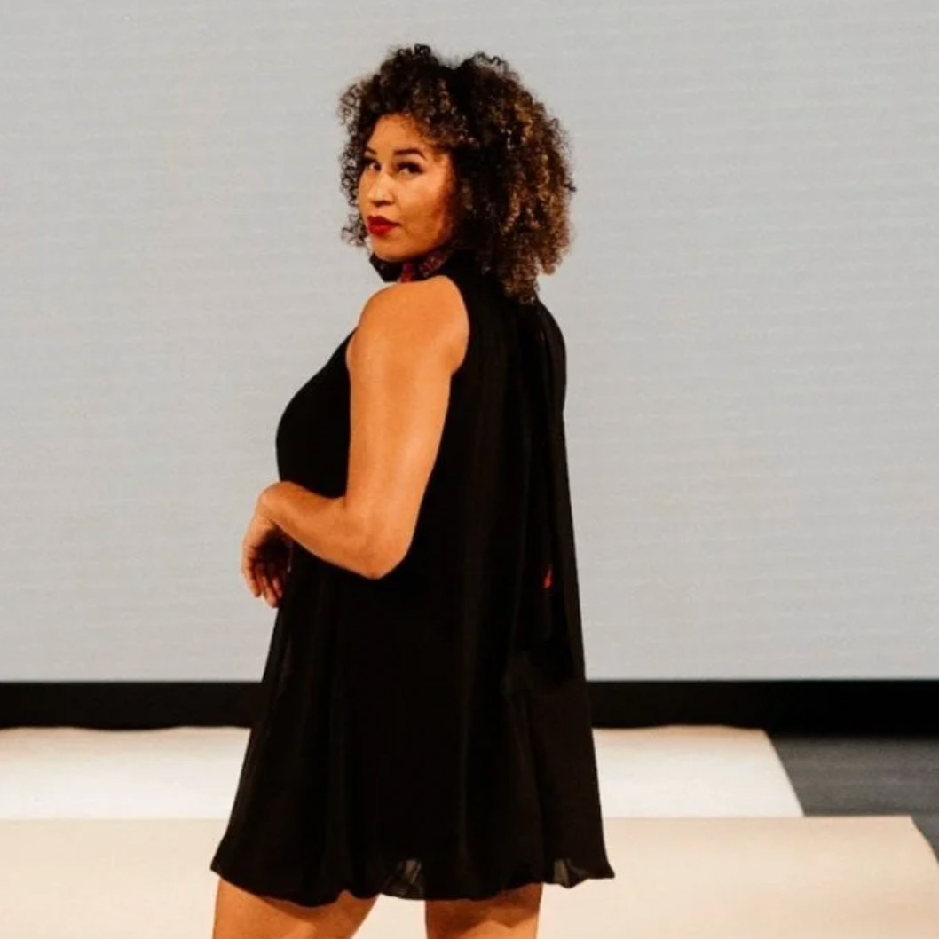 Woman facing left wearing a black sleeveless dress against a plain background