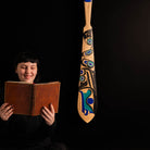 Person holding a book next to a large, intricately designed wooden paddle on a black background