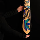 Person hands beside a wooden paddle with intricate carvings against a black background.