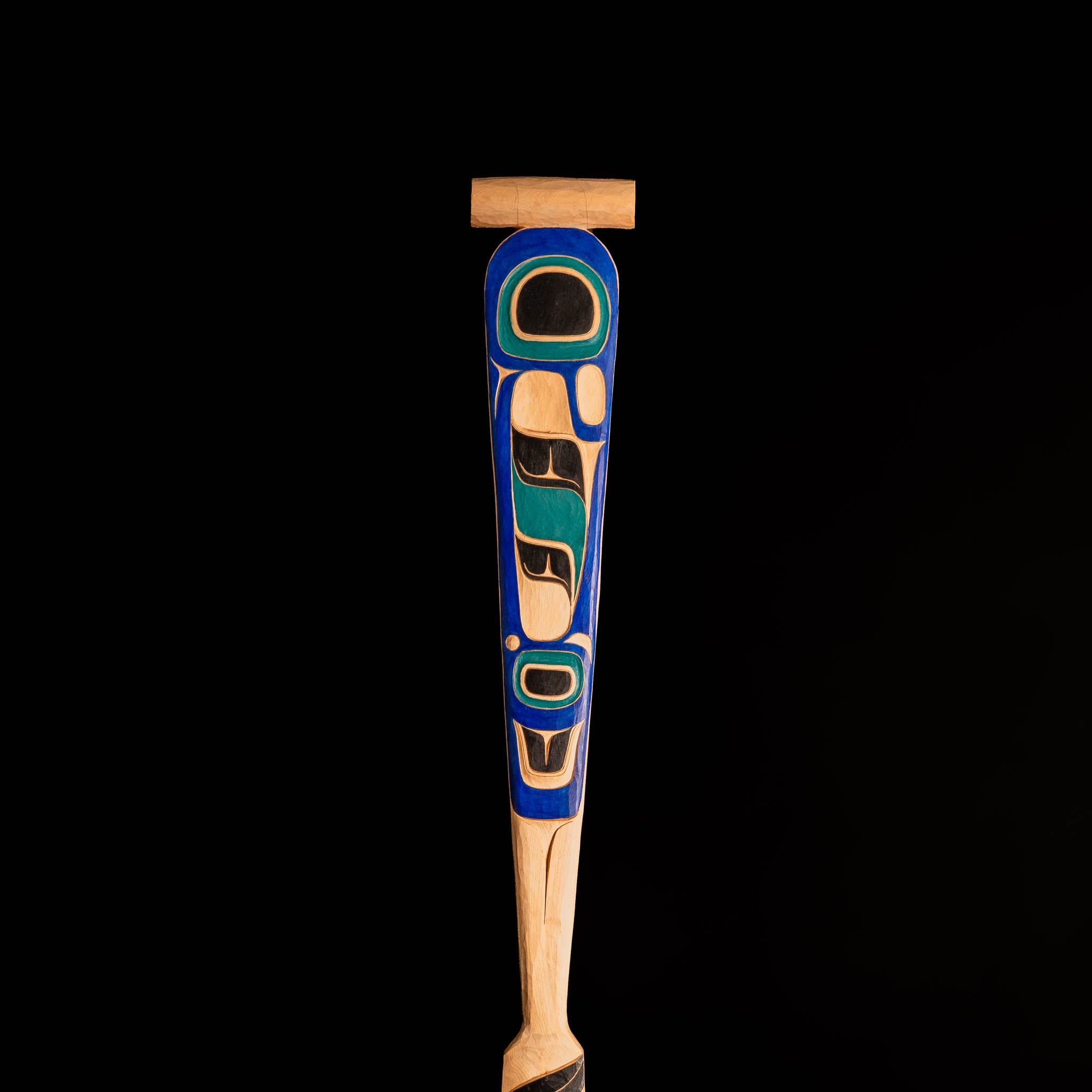 Wooden carved paddle with blue and black painted design on a black background.